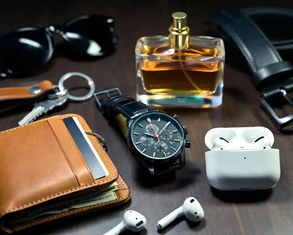 Collection of  accessories including wallet, watch, sunglasses, keychain, and airpods on a wooden surface.